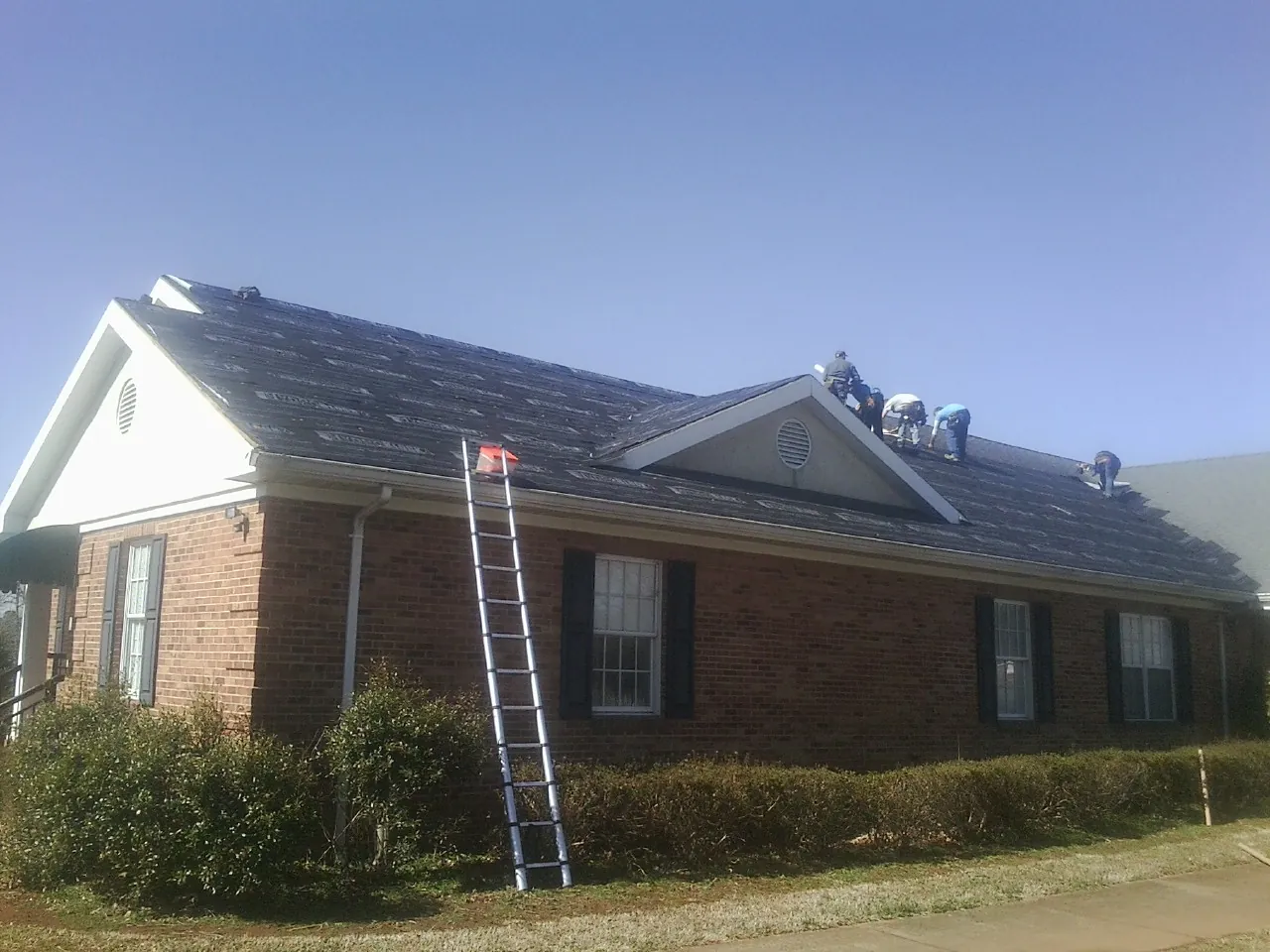 Crew tearing shingles off a brick ranch roof with a ladder set — Metal Roof Repair work by our crew in Shickshinny
