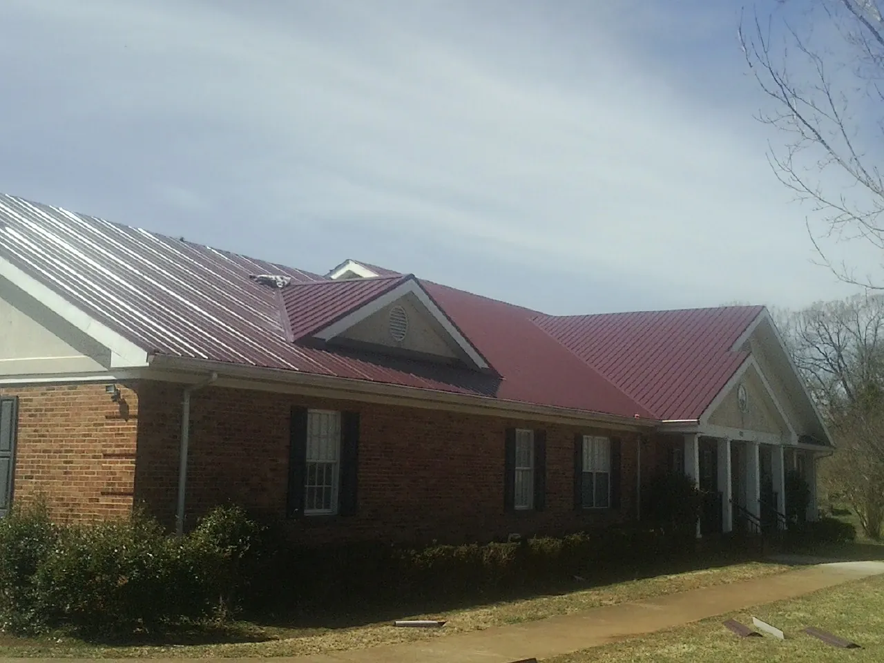 Red metal roof with gabled entries on a long brick building, from a Hail Damage Roof Repair job in Shickshinny