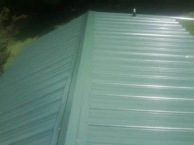 New green metal panels meeting at the ridge of a roof — Flat Roof Repair work by our crew in Shickshinny