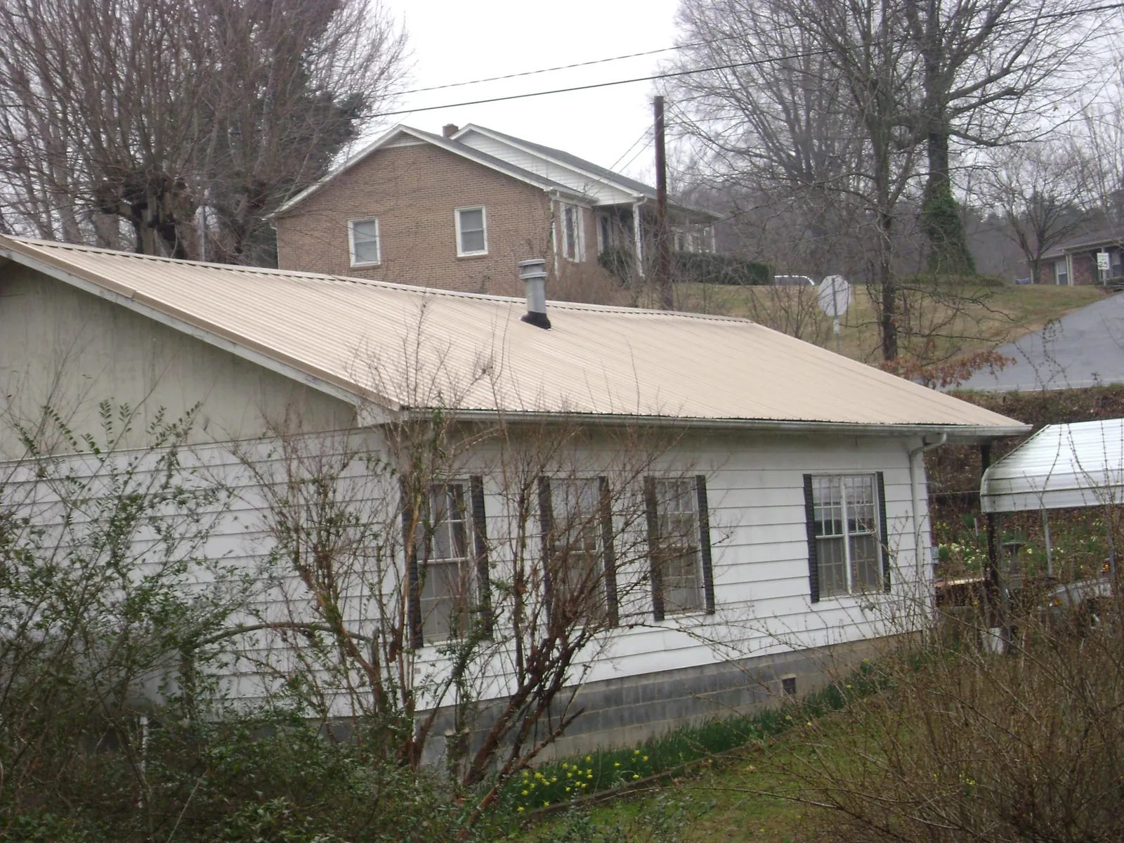 Tan metal roof on a white sided house set into a hillside — Commercial Roofing by Roofing Brothers in Shickshinny